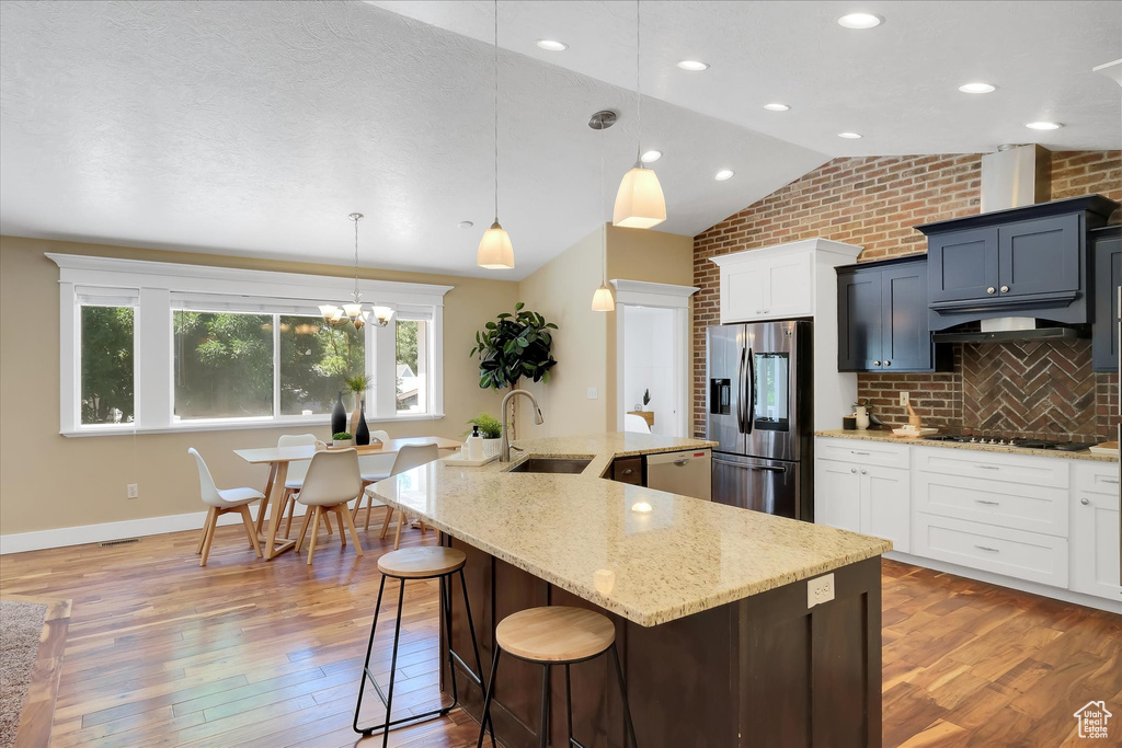 Kitchen with stainless steel fridge, a large island with sink, light wood-style floors, light stone countertops, and a kitchen bar