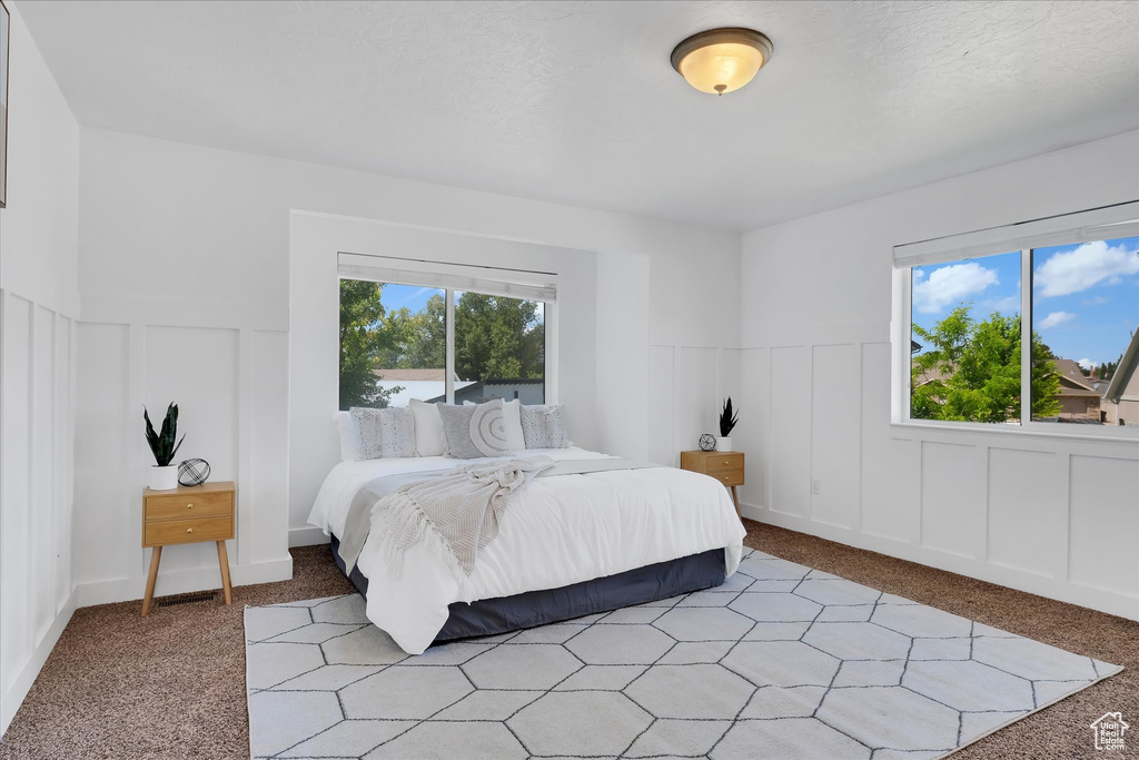 Bedroom with a decorative wall, light carpet, and wainscoting