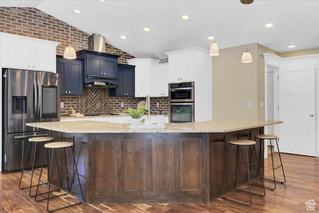 Kitchen featuring stainless steel appliances, lofted ceiling, decorative backsplash, a kitchen breakfast bar, and dark wood-style flooring