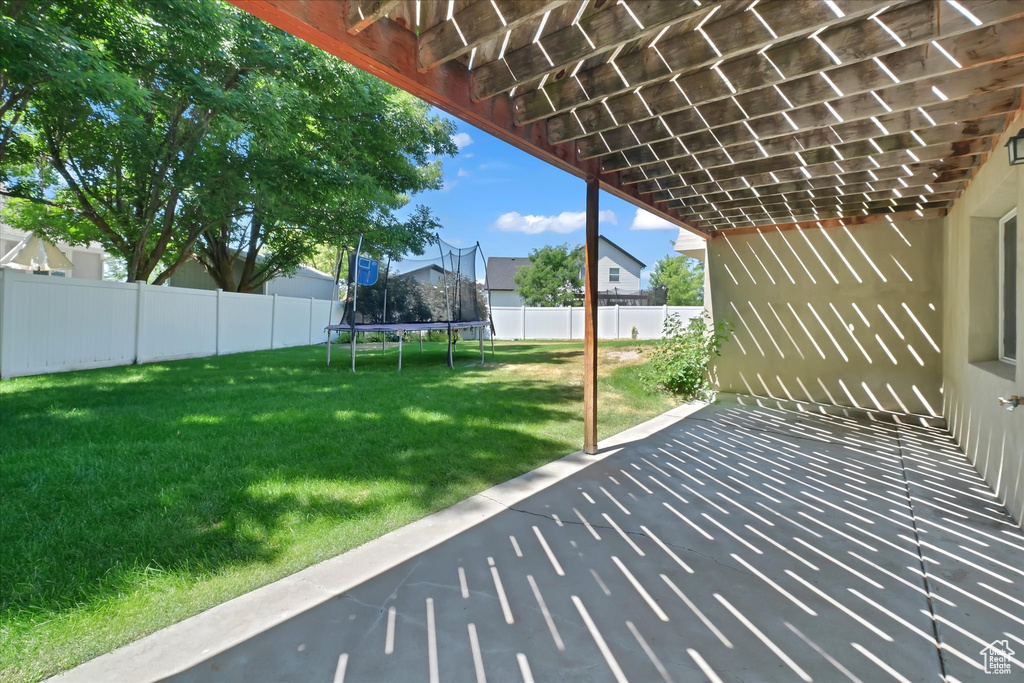 Fenced backyard featuring a trampoline and a patio