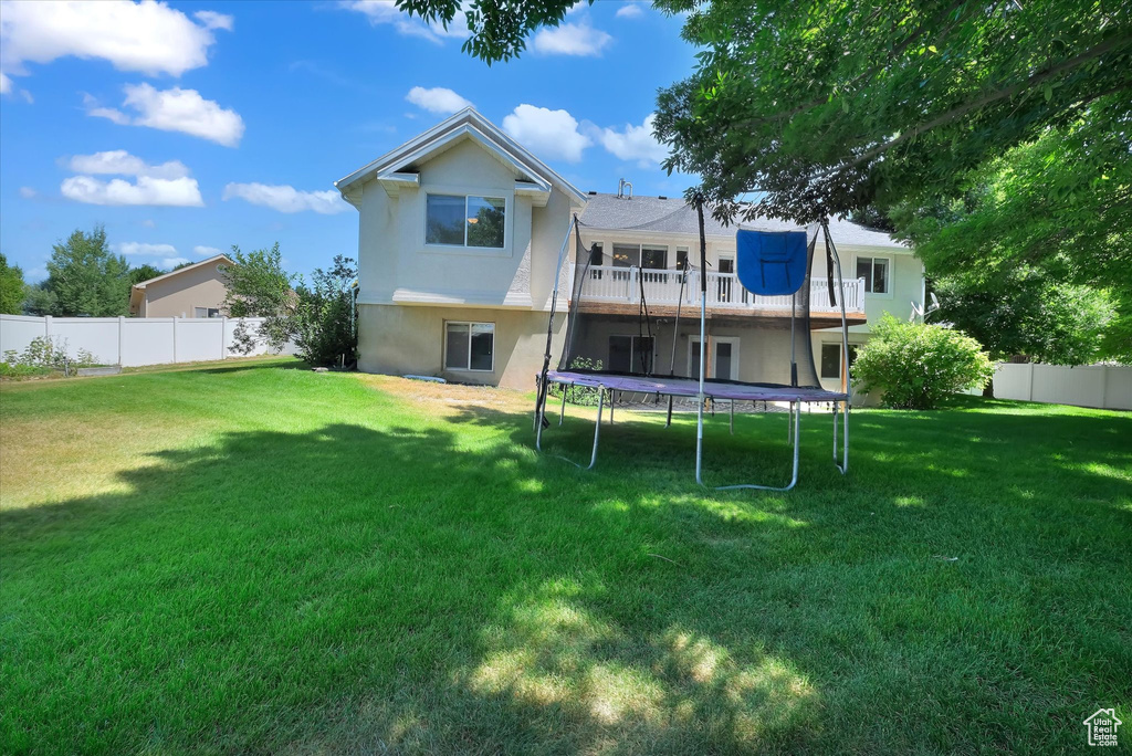 Rear view of property with a trampoline, stucco siding, a fenced backyard, and a deck