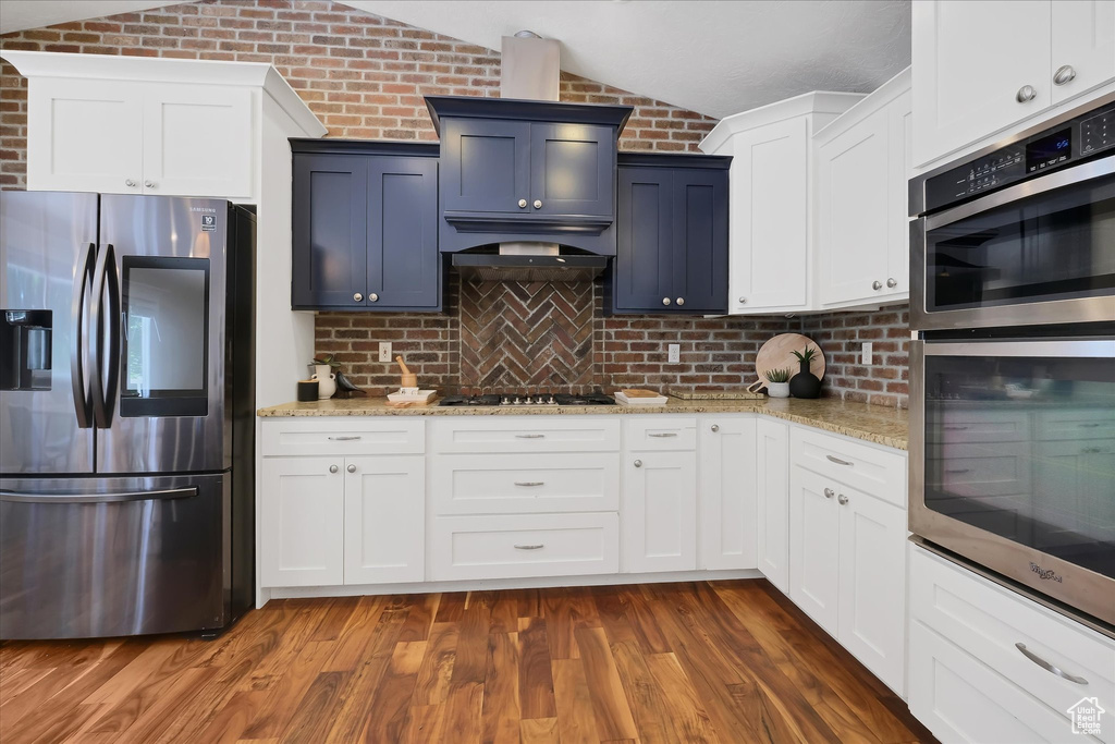 Kitchen with stainless steel appliances, vaulted ceiling, tasteful backsplash, light stone countertops, and dark wood-style floors