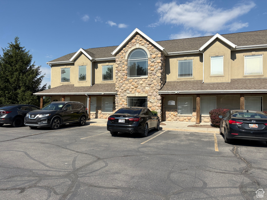 Townhome / multi-family property featuring uncovered parking, stucco siding, roof with shingles, and stone siding