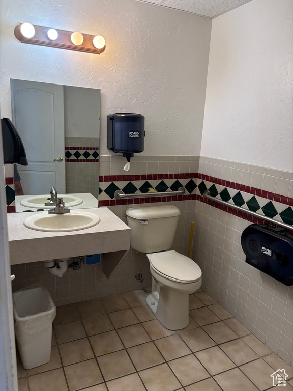 Half bathroom featuring tile walls, tile patterned floors, a wainscoted wall, and a textured wall