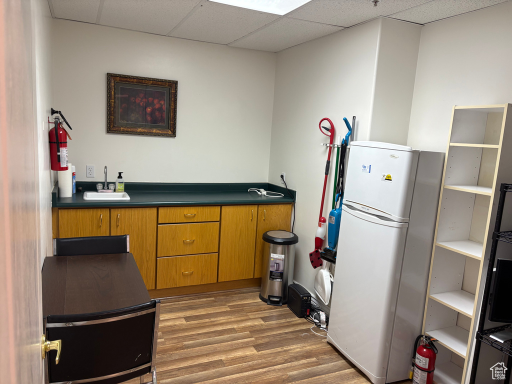 Kitchen with freestanding refrigerator, brown cabinets, wood finished floors, dark countertops, and a drop ceiling