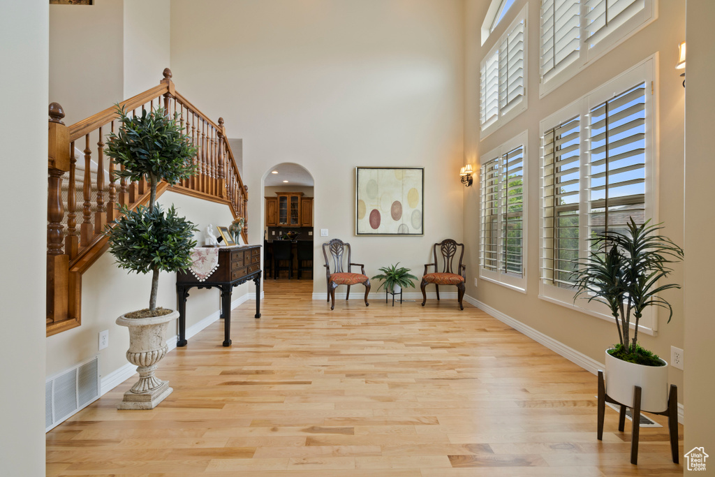 Foyer entrance with a towering ceiling, arched walkways, light wood finished floors, and stairway