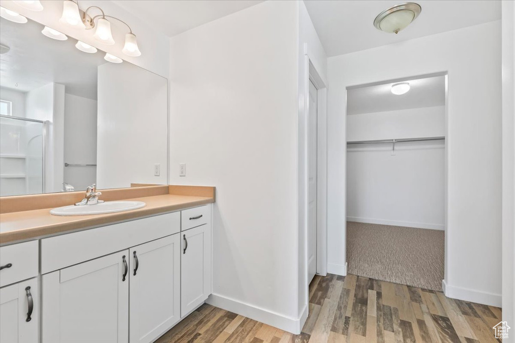 Full bathroom with vanity, a walk in closet, wood finished floors, and a shower