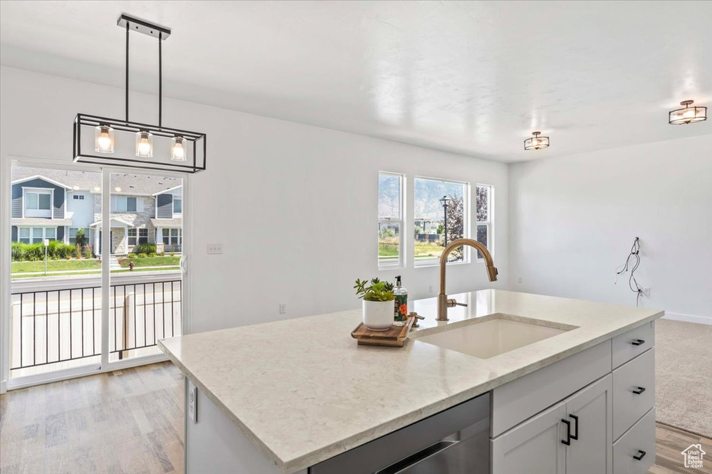 Kitchen with dishwasher, light wood finished floors, light stone countertops, pendant lighting, and an island with sink