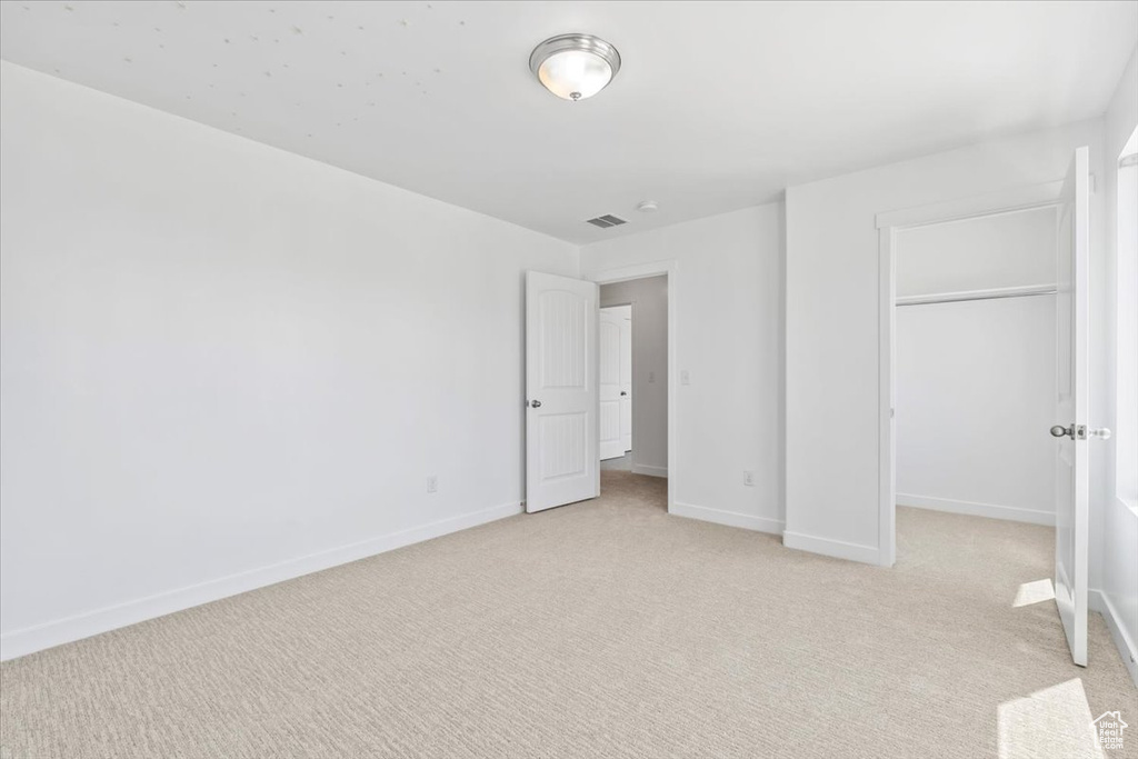 Unfurnished bedroom with light colored carpet, a closet, and a walk in closet