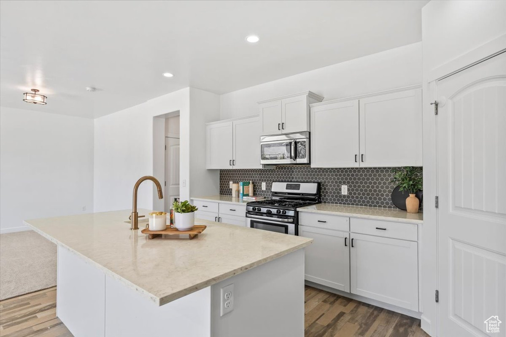 Kitchen with appliances with stainless steel finishes, tasteful backsplash, an island with sink, white cabinetry, and light wood finished floors
