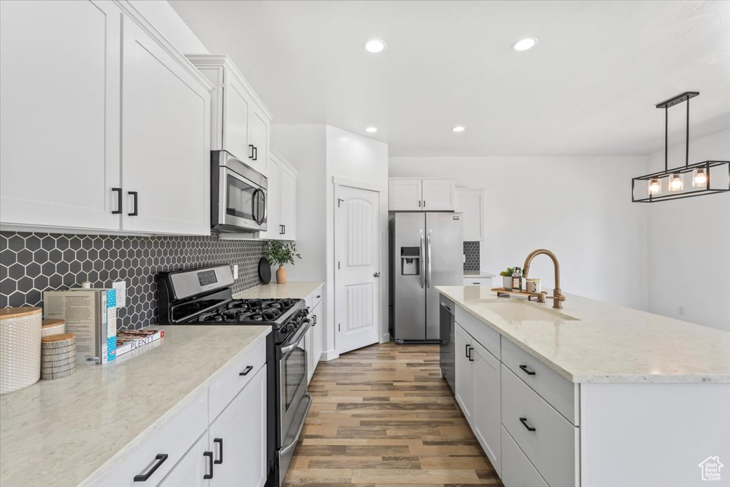 Kitchen featuring stainless steel appliances, light wood-style floors, backsplash, white cabinetry, and a center island with sink
