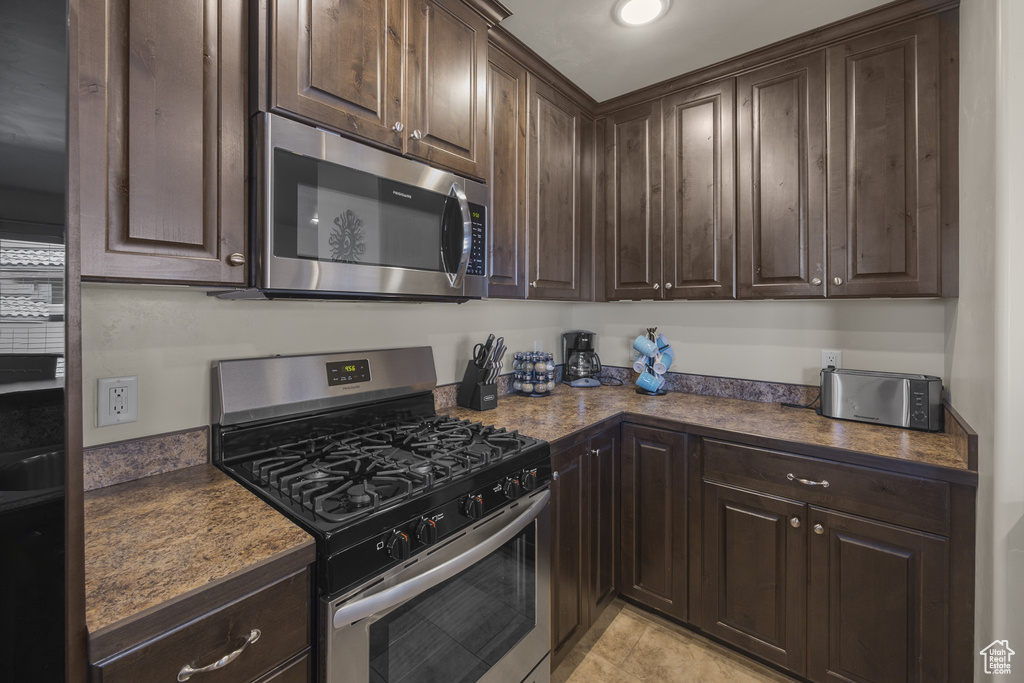 Kitchen with appliances with stainless steel finishes, dark brown cabinetry, and light tile patterned floors