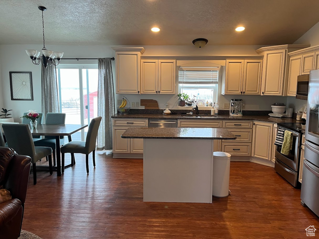 Kitchen with appliances with stainless steel finishes, a chandelier, a center island, dark wood-style flooring, and a textured ceiling