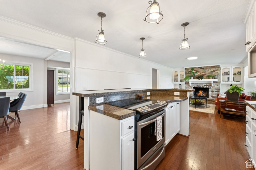 Kitchen featuring stainless steel electric range oven, a kitchen bar, a large fireplace, dark countertops, and dark wood-type flooring