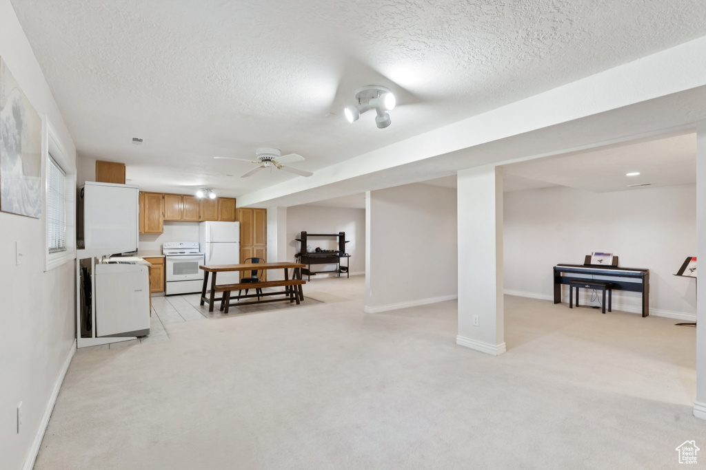 Finished basement with freestanding refrigerator, a textured ceiling, light colored carpet, and a ceiling fan