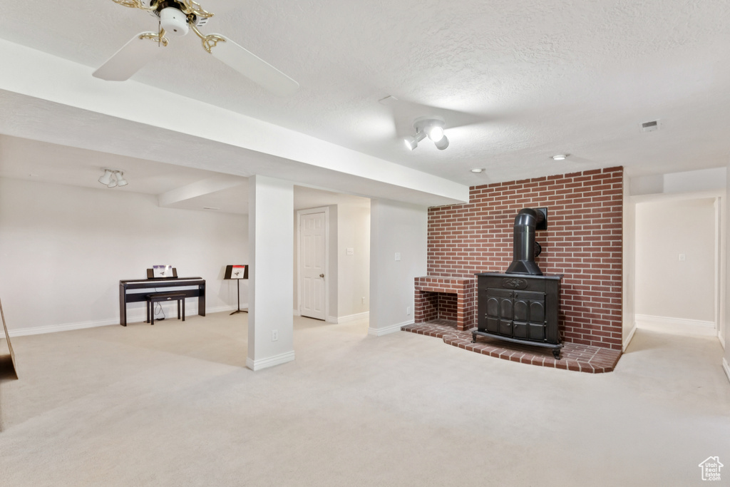 Unfurnished living room featuring carpet, a wood stove, a textured ceiling, and ceiling fan