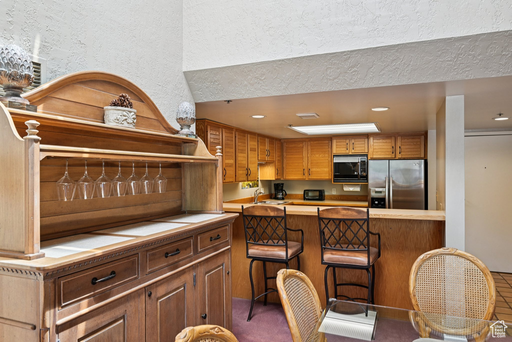 Kitchen featuring stainless steel refrigerator with ice dispenser, black microwave, a breakfast bar, light countertops, and recessed lighting