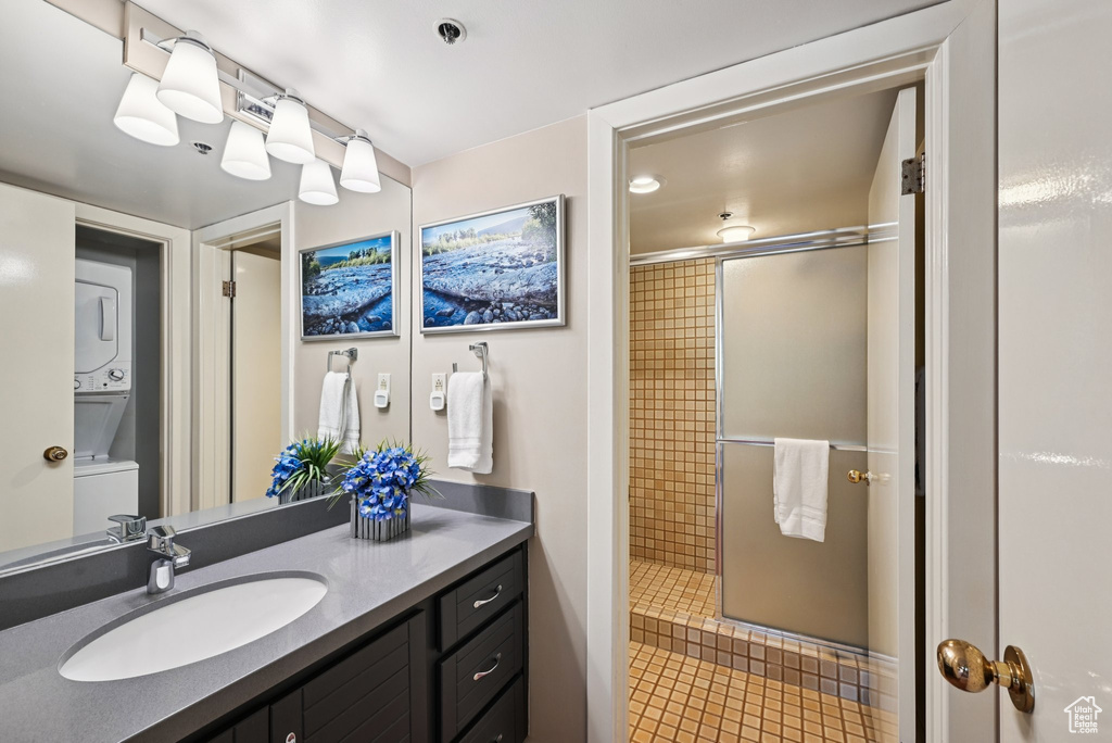 Full bathroom with stacked washer / drying machine, vanity, tiled shower, and tile patterned flooring