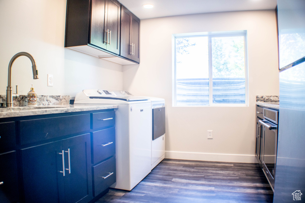 Washroom featuring washing machine and clothes dryer, cabinet space, and dark wood-style flooring