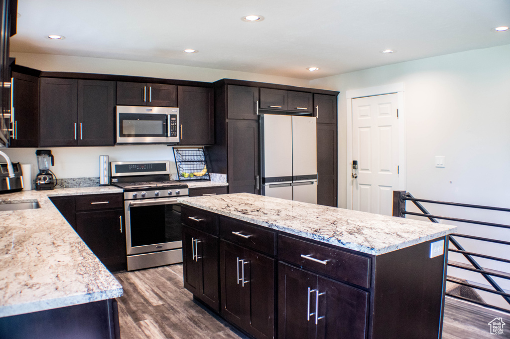 Kitchen with appliances with stainless steel finishes, dark wood finished floors, a kitchen island, recessed lighting, and light stone countertops