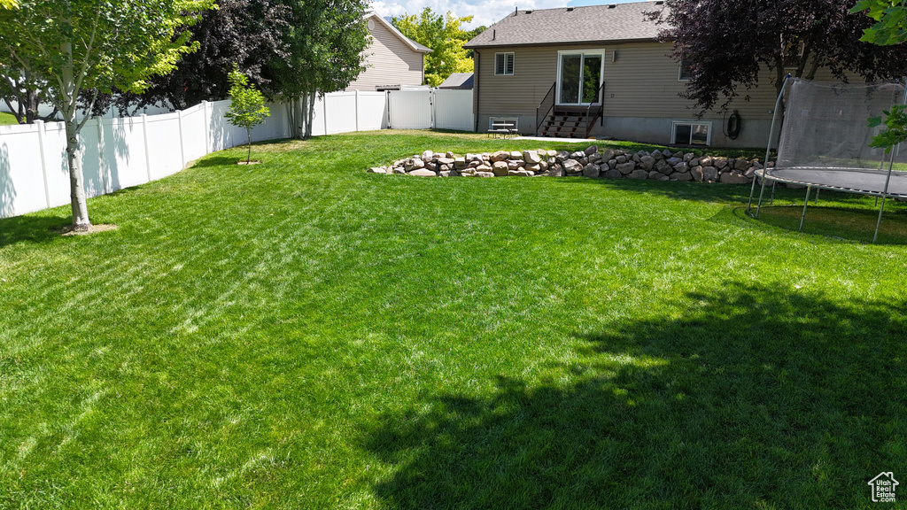 Fenced backyard featuring a trampoline and entry steps