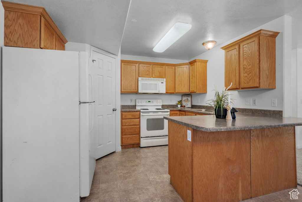 Kitchen featuring white appliances, a peninsula, dark countertops, and brown cabinetry