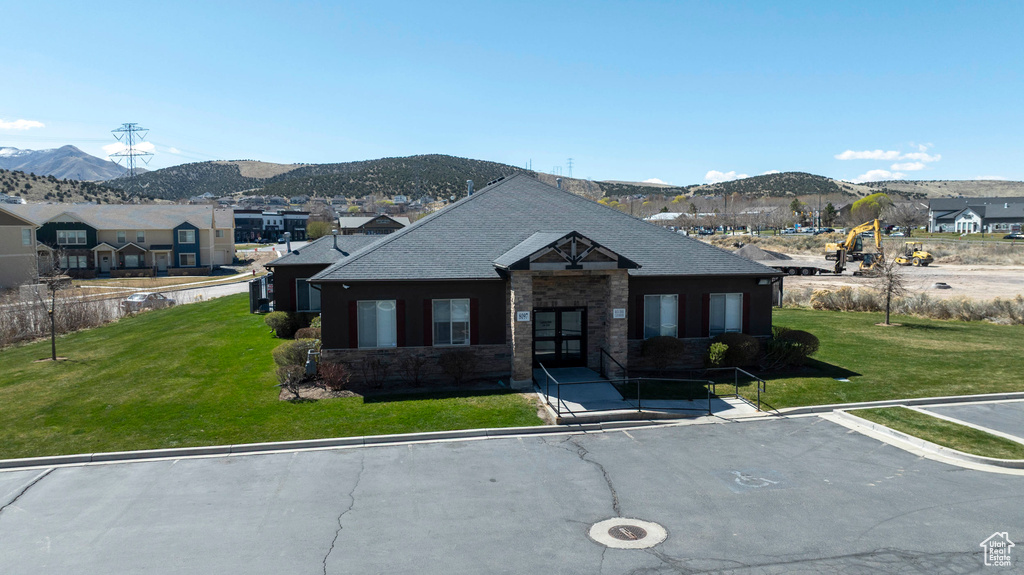 View of front facade featuring a mountain view, a front lawn, roof with shingles, and a residential view