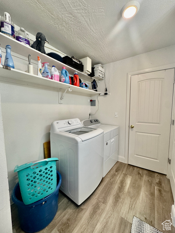 Laundry area with independent washer and dryer, light wood finished floors, and a textured ceiling