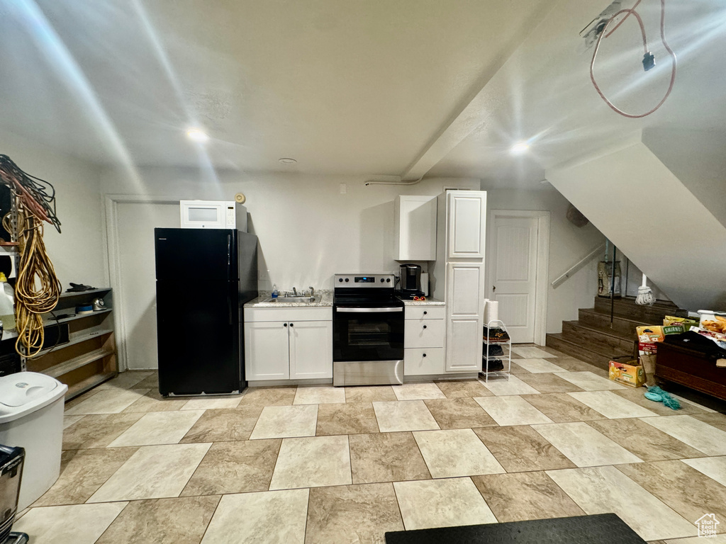 Kitchen featuring stainless steel range with electric cooktop, freestanding refrigerator, white cabinets, light countertops, and stone finish flooring