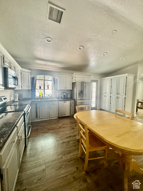 Kitchen with stainless steel appliances, a textured ceiling, dark countertops, dark wood finished floors, and white cabinets