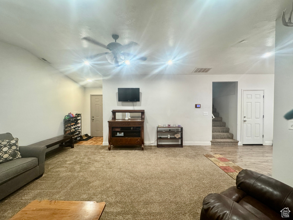 Carpeted living area featuring ceiling fan and stairway