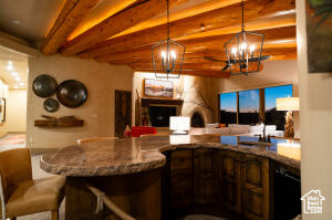 Kitchen with beam ceiling, a chandelier, open floor plan, decorative light fixtures, and stone counters