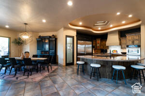 Kitchen featuring custom range hood, fridge, stainless steel double oven, a kitchen breakfast bar, and recessed lighting