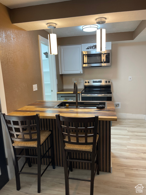 Kitchen featuring appliances with stainless steel finishes, light wood-style floors, and decorative light fixtures
