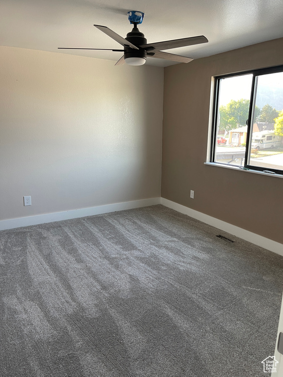 Carpeted empty room featuring ceiling fan and baseboards