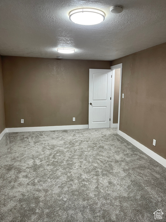 Carpeted empty room featuring a textured ceiling and a smoke detector