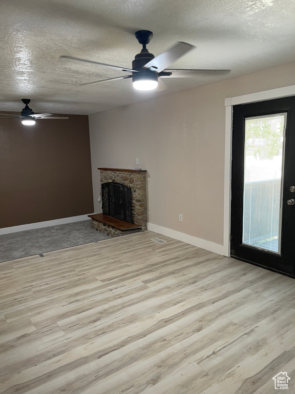 Unfurnished living room with a ceiling fan, a textured ceiling, light wood-style flooring, and a stone fireplace