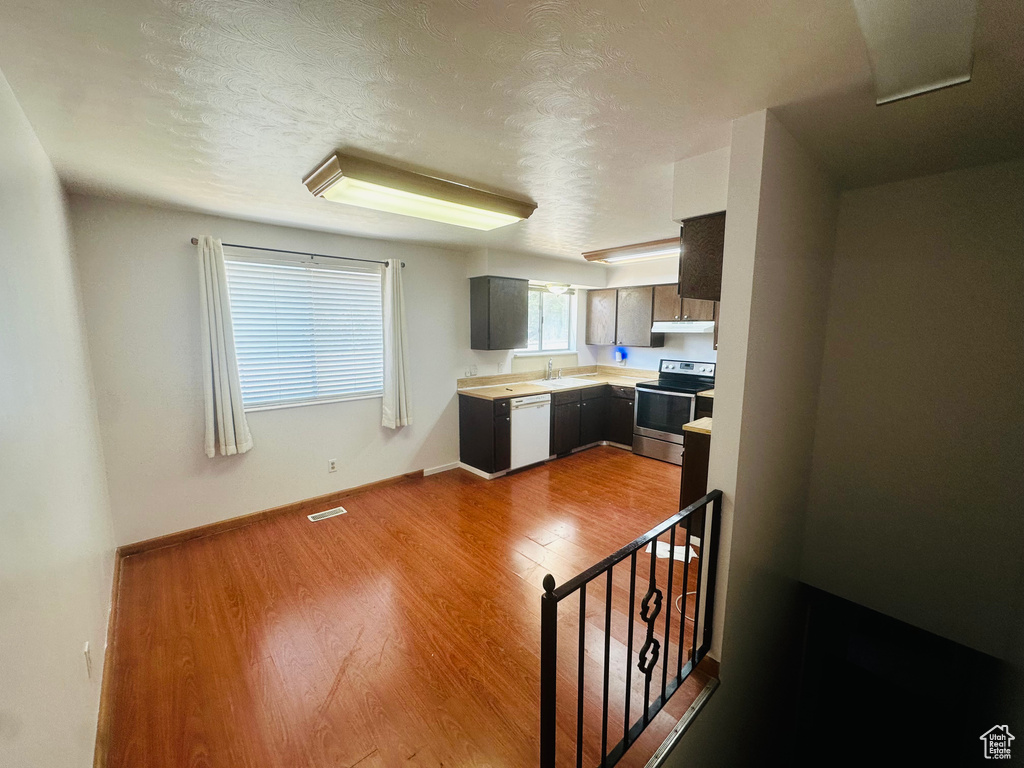 Kitchen with stainless steel range with electric cooktop, white dishwasher, under cabinet range hood, light countertops, and wood finished floors