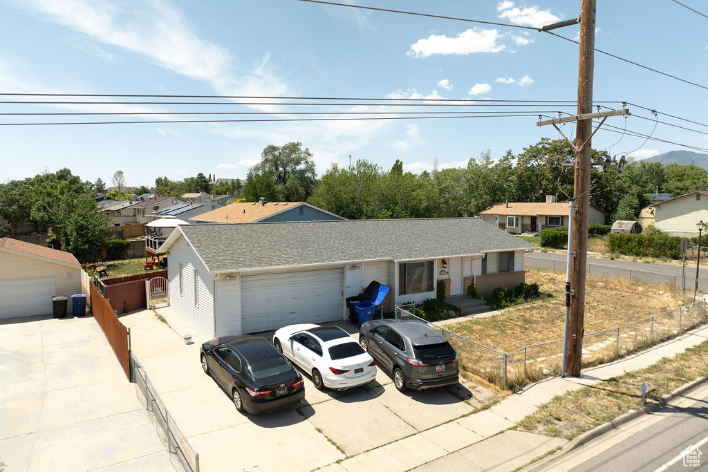 Ranch-style home featuring concrete driveway, a garage, a fenced front yard, roof with shingles, and a residential view