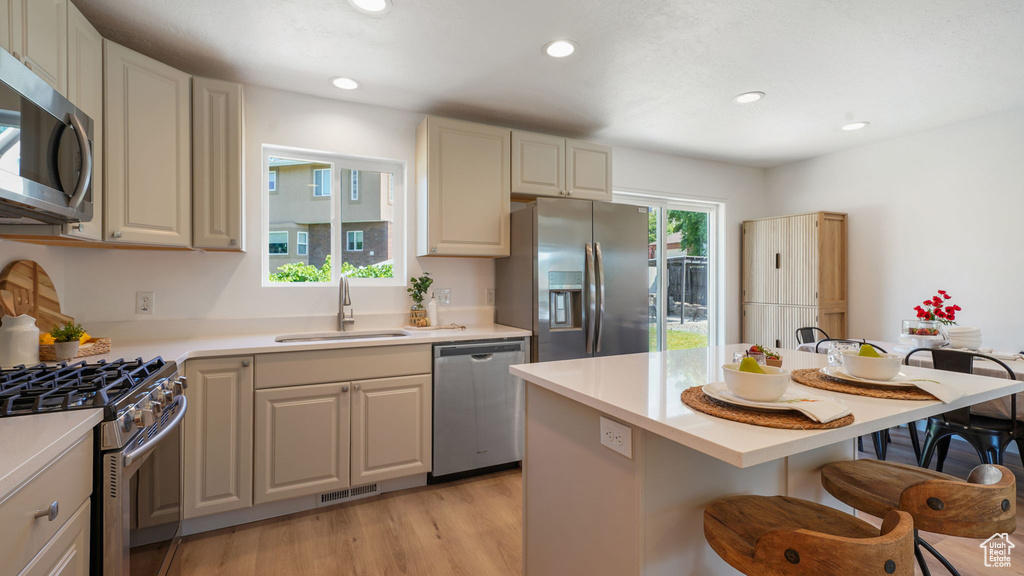 Kitchen with appliances with stainless steel finishes, a kitchen bar, light countertops, light wood finished floors, and recessed lighting