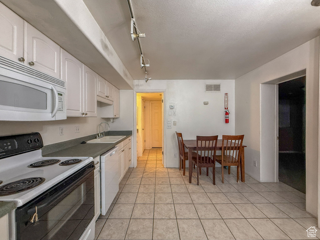 Kitchen featuring white appliances, white cabinetry, track lighting, light tile patterned floors, and dark countertops