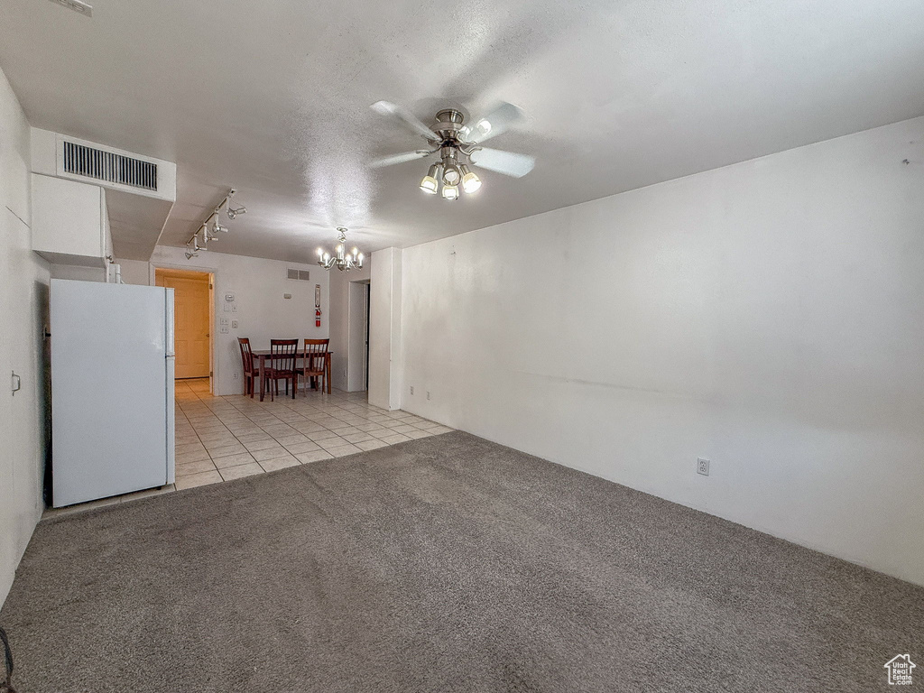 Carpeted spare room with ceiling fan, tile patterned flooring, and a chandelier