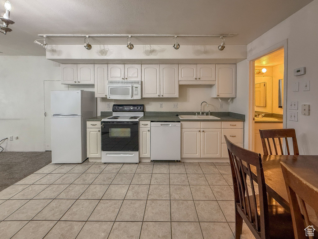Kitchen with white appliances, dark countertops, track lighting, light tile patterned floors, and white cabinets