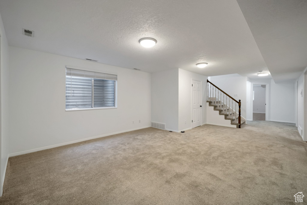 Basement with stairs, light carpet, and a textured ceiling