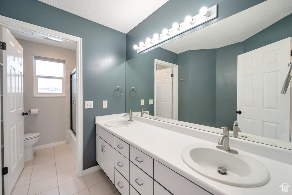 Full bath with double vanity, tile patterned flooring, and shower / bath combination with glass door