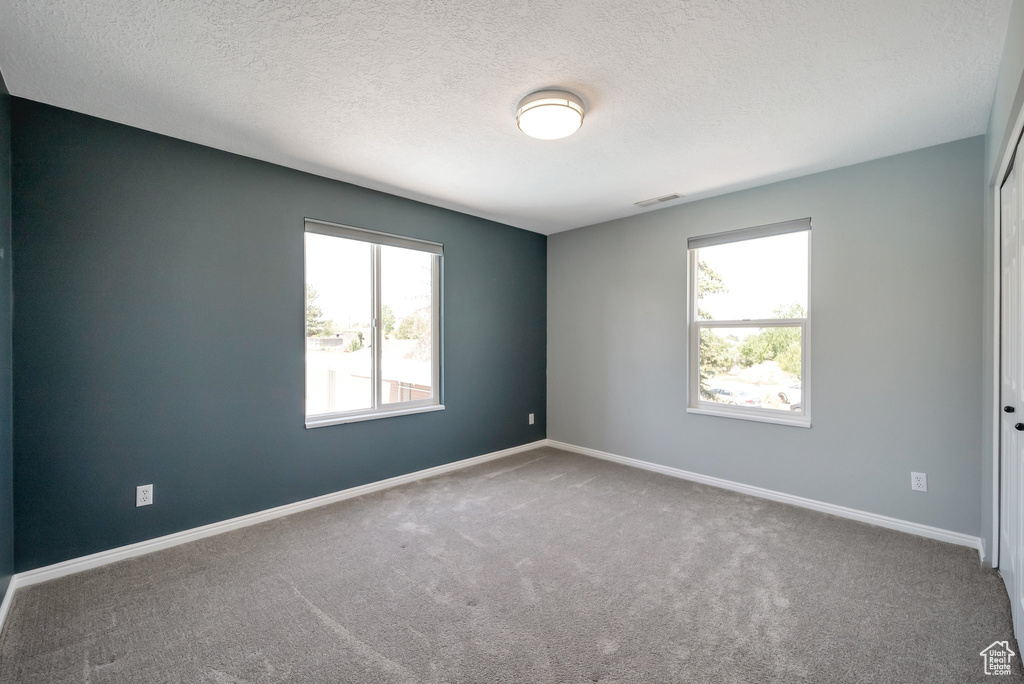 Carpeted empty room with a textured ceiling and baseboards