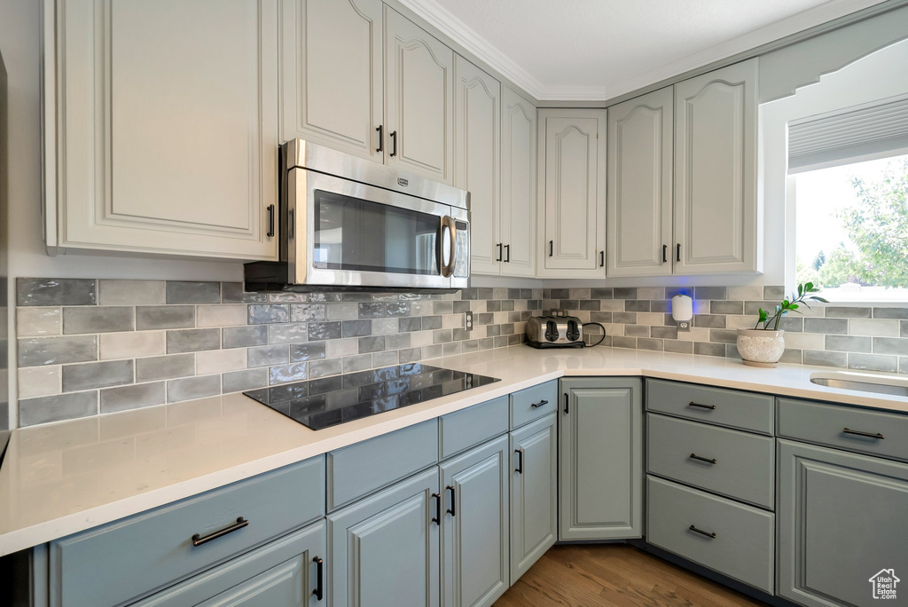 Kitchen with stainless steel microwave, black electric cooktop, light countertops, and gray cabinetry