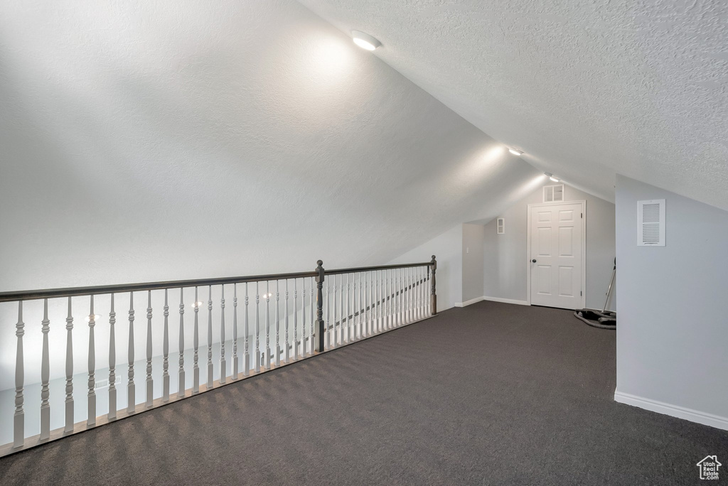 Additional living space featuring lofted ceiling, dark colored carpet, and a textured ceiling