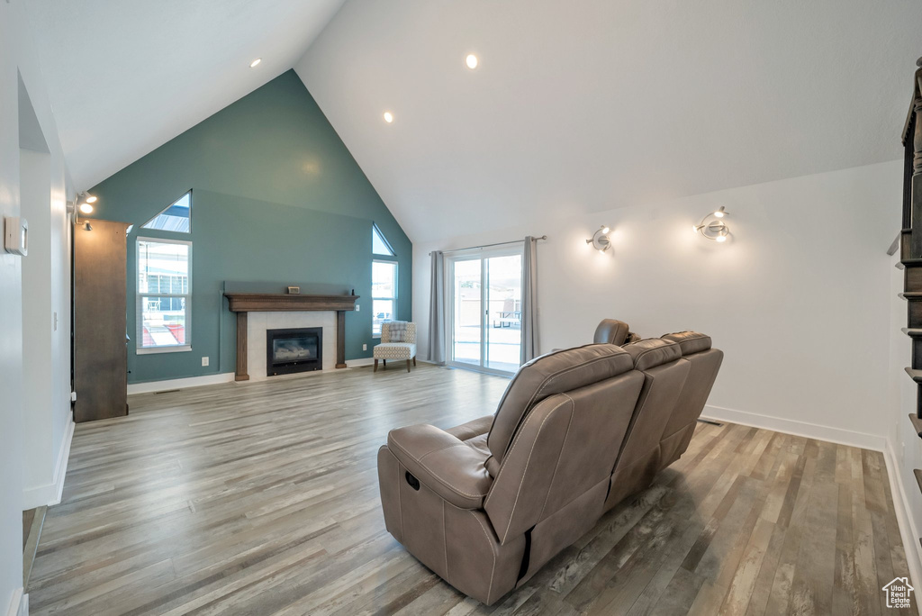 Living room with a glass covered fireplace, light wood finished floors, high vaulted ceiling, and recessed lighting