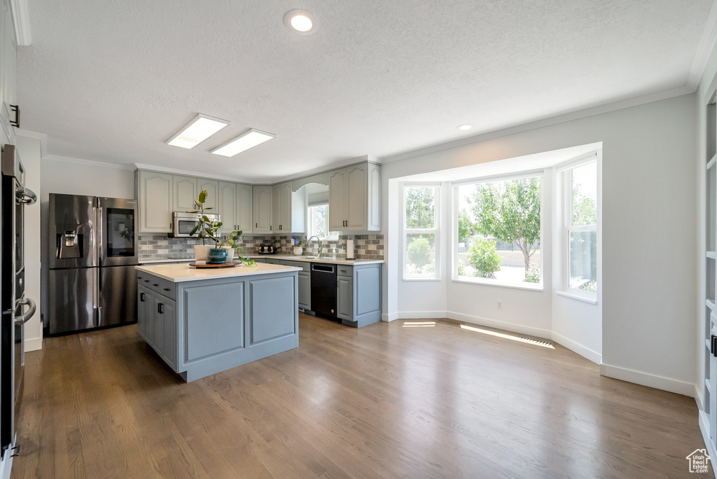 Kitchen with stainless steel appliances, gray cabinets, tasteful backsplash, light countertops, and ornamental molding